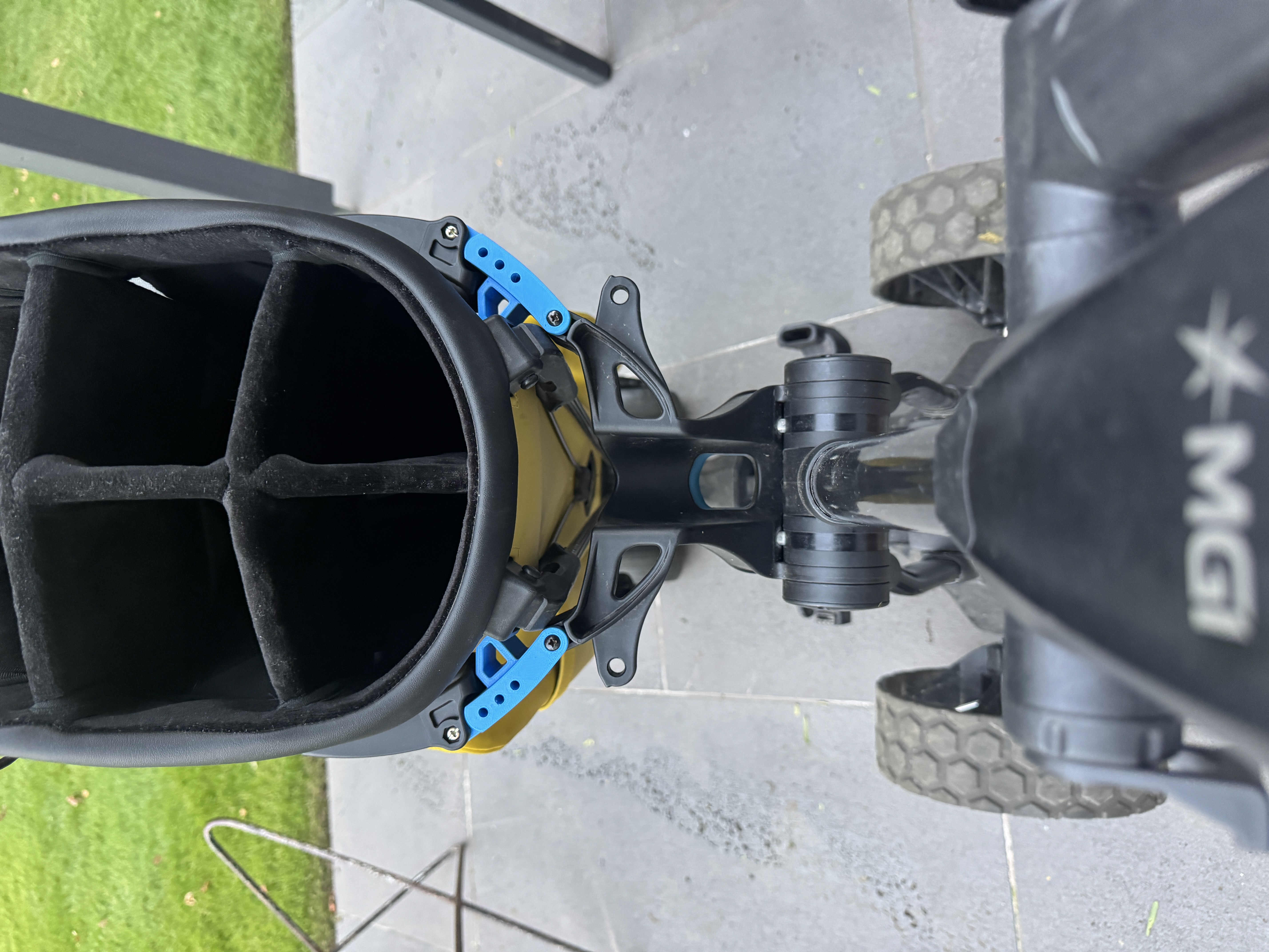 Overhead view of blue 3D-printed MGI golf bag fasteners securing a yellow stand bag to a black trolley